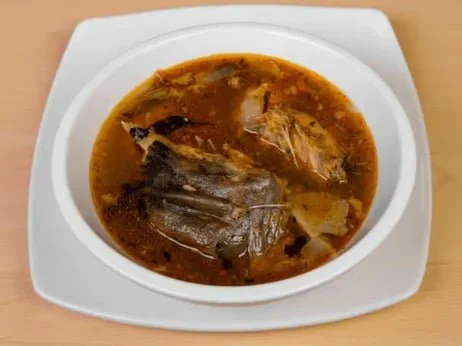 Fish head soup in a white bowl on a wooden surface