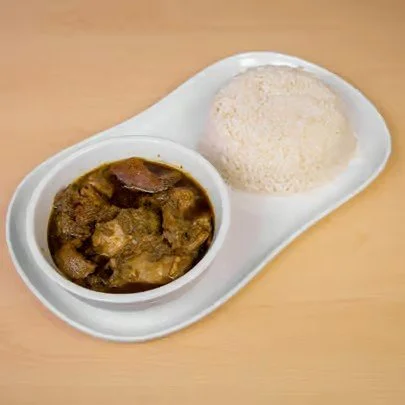 A plate with a serving of white rice and a bowl of beef stew on a wooden table.