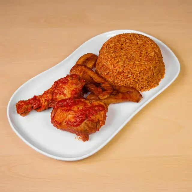Plate with fried chicken drumsticks, fried plantains, crispy bacon, and a mound of seasoned rice.