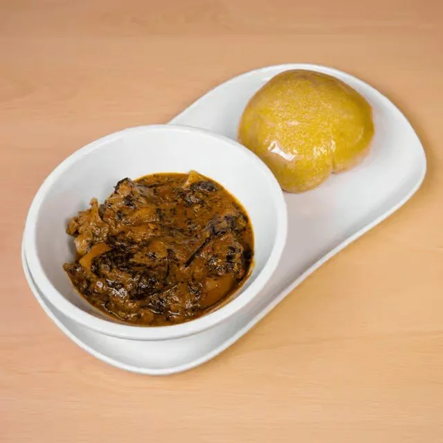 A white plate with a bowl of Indian-style curry and a round piece of bread on a wooden table.