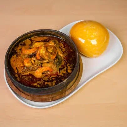 A bowl of spicy shrimp curry with a yellow bread roll on a white plate.