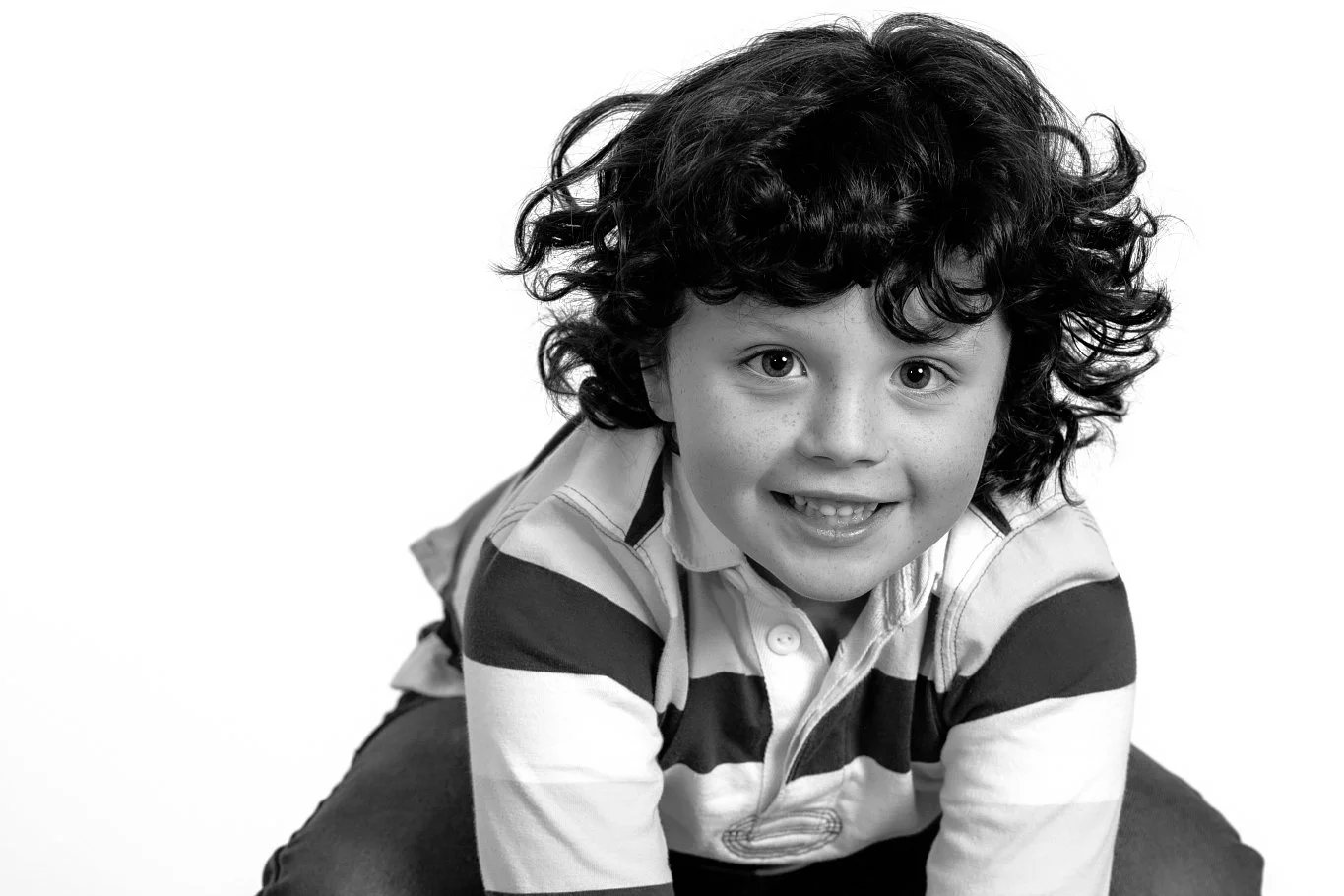 Black and white photo of a young boy with curly hair smiling and looking at the camera, wearing a striped shirt.