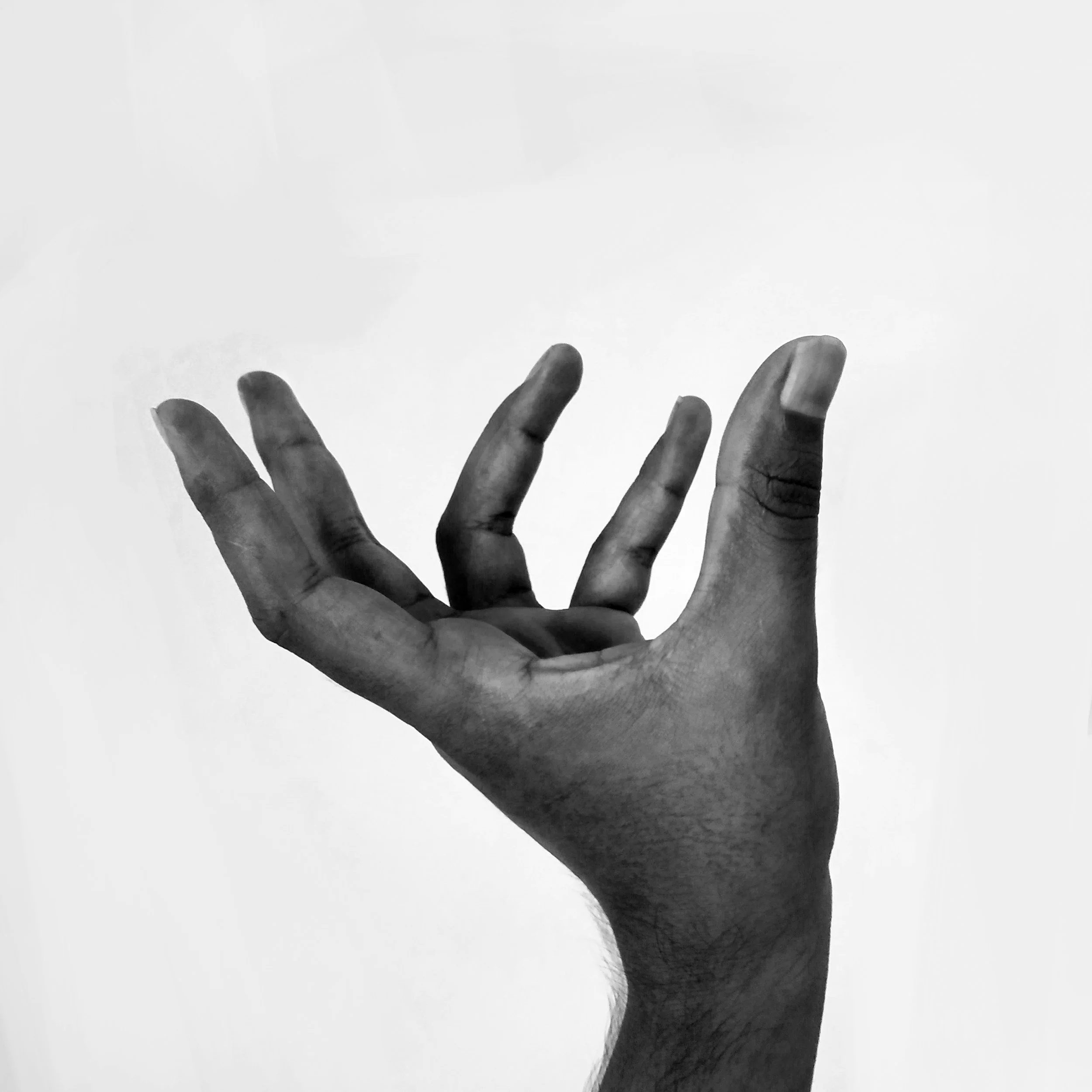 A black and white photo of a human hand with fingers slightly spread, positioned against a plain light-colored background.