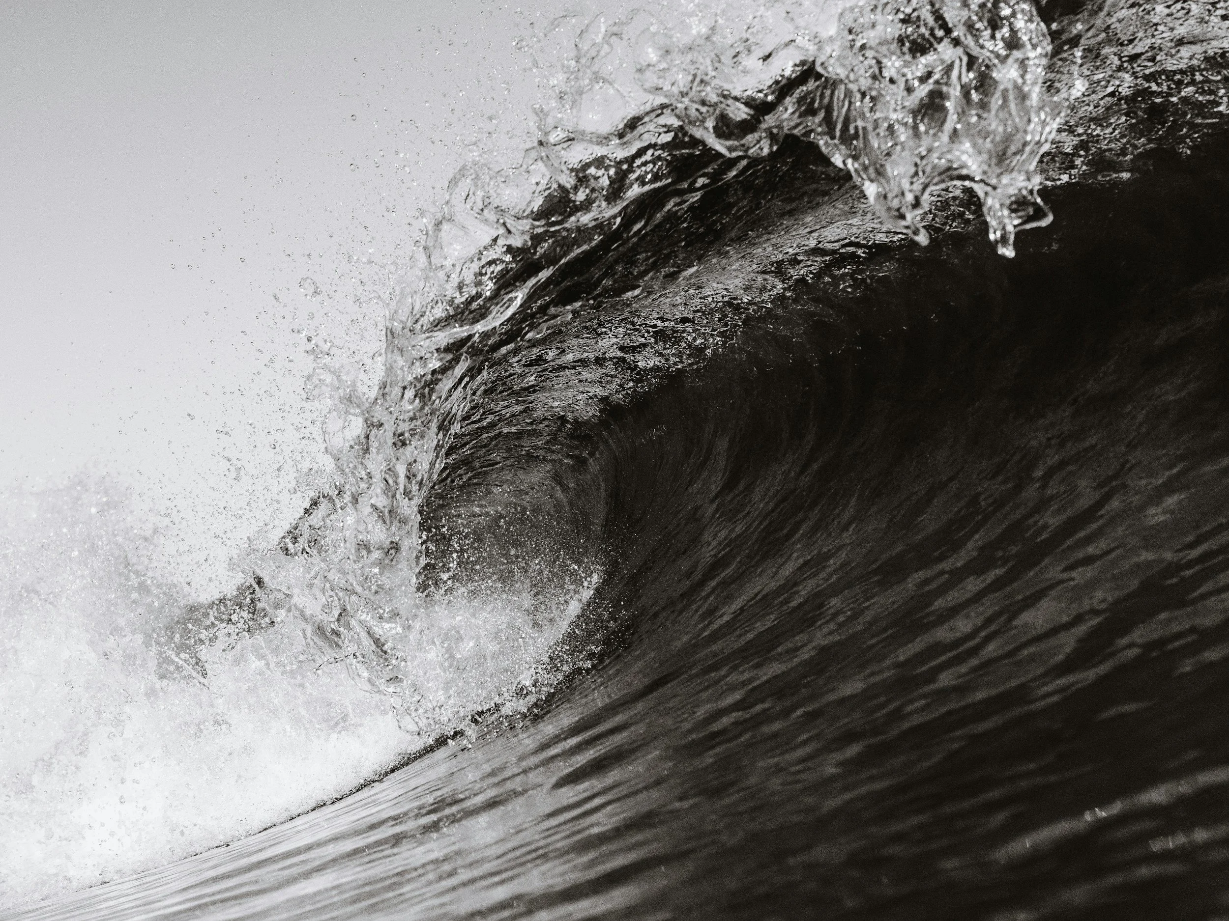 A close-up of a water wave crashing against a dark surface, with visible water droplets and foam.
