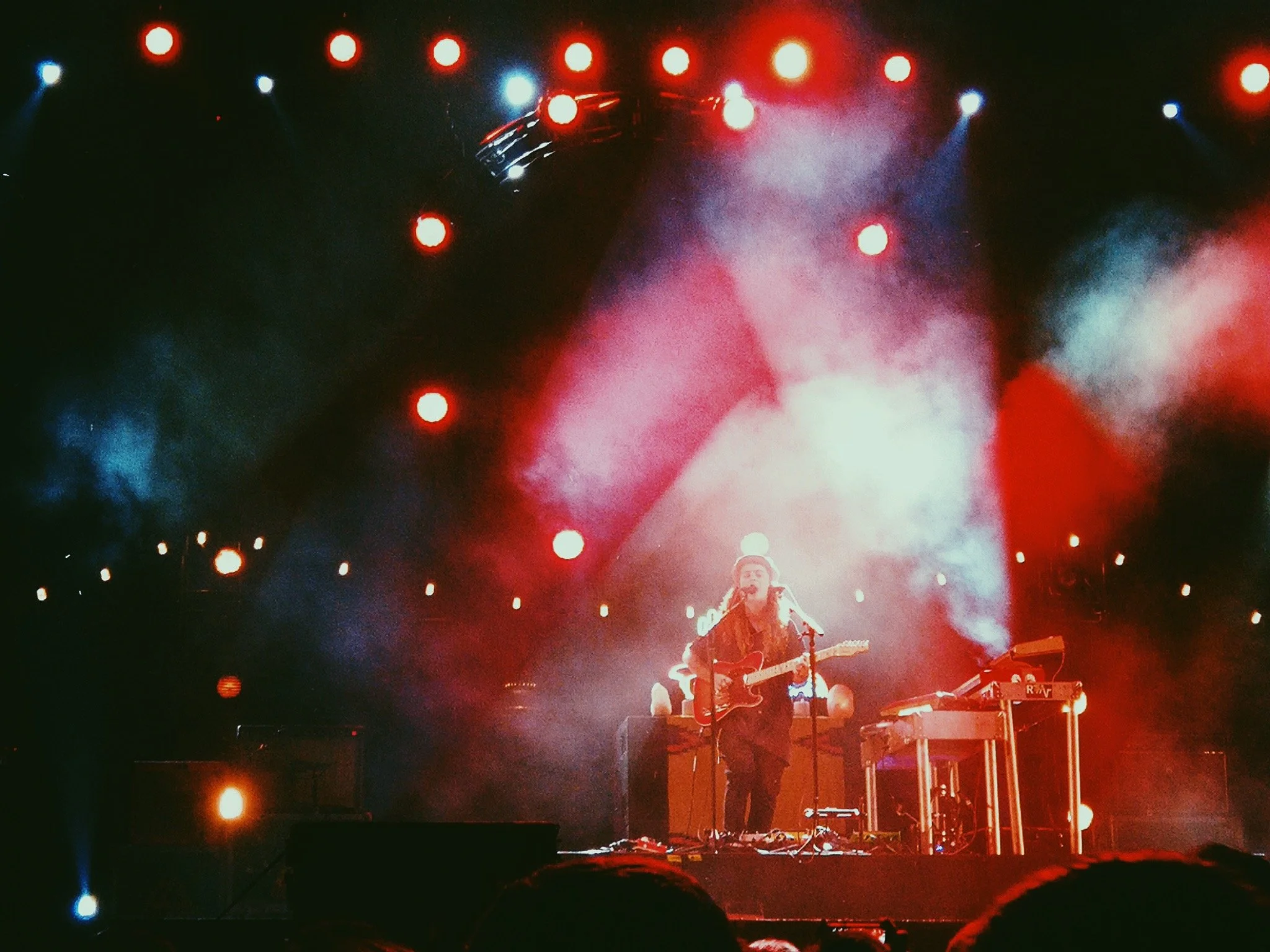 A musician performing on stage at night, playing an acoustic guitar and singing into a microphone, with colorful stage lights and smoke effects.
