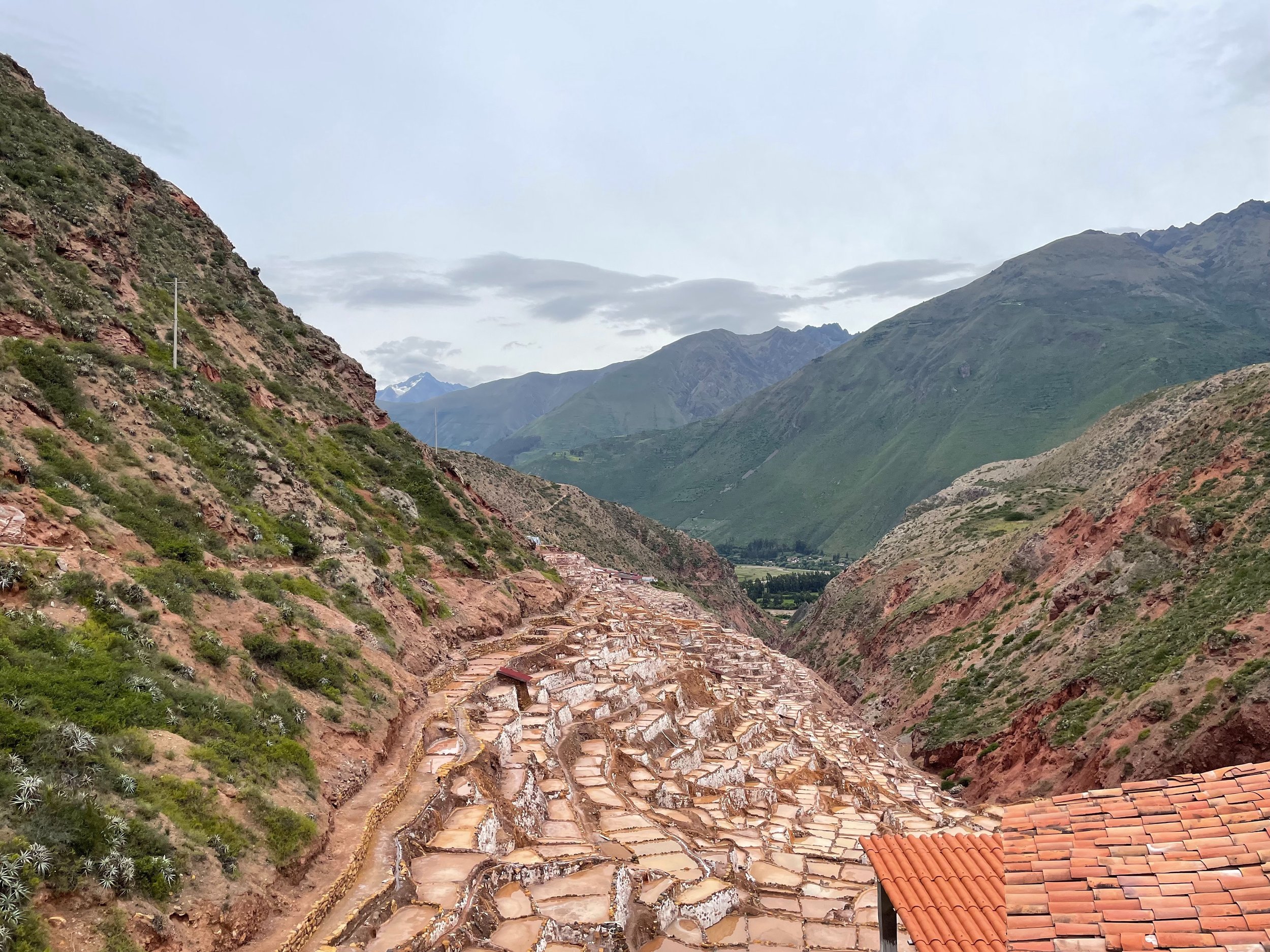 Salt evaporation ponds in a mountainous area with terraced levels and a small town at the bottom, under a sky with some clouds.