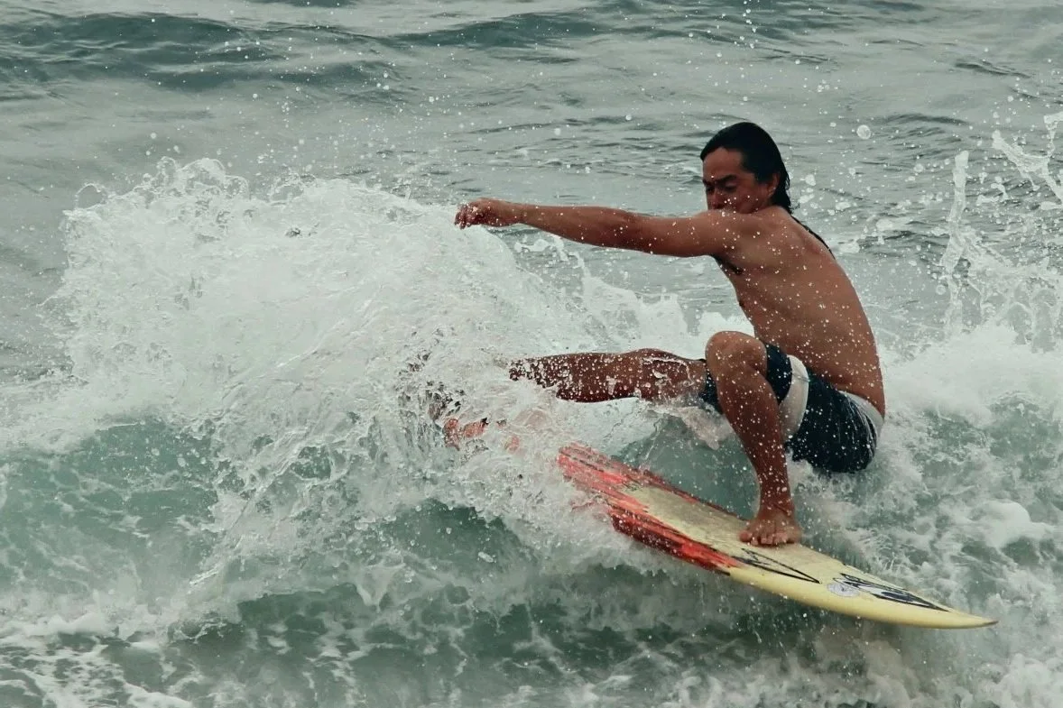 A man surfing on a wave in the ocean, wearing black swim trunks.