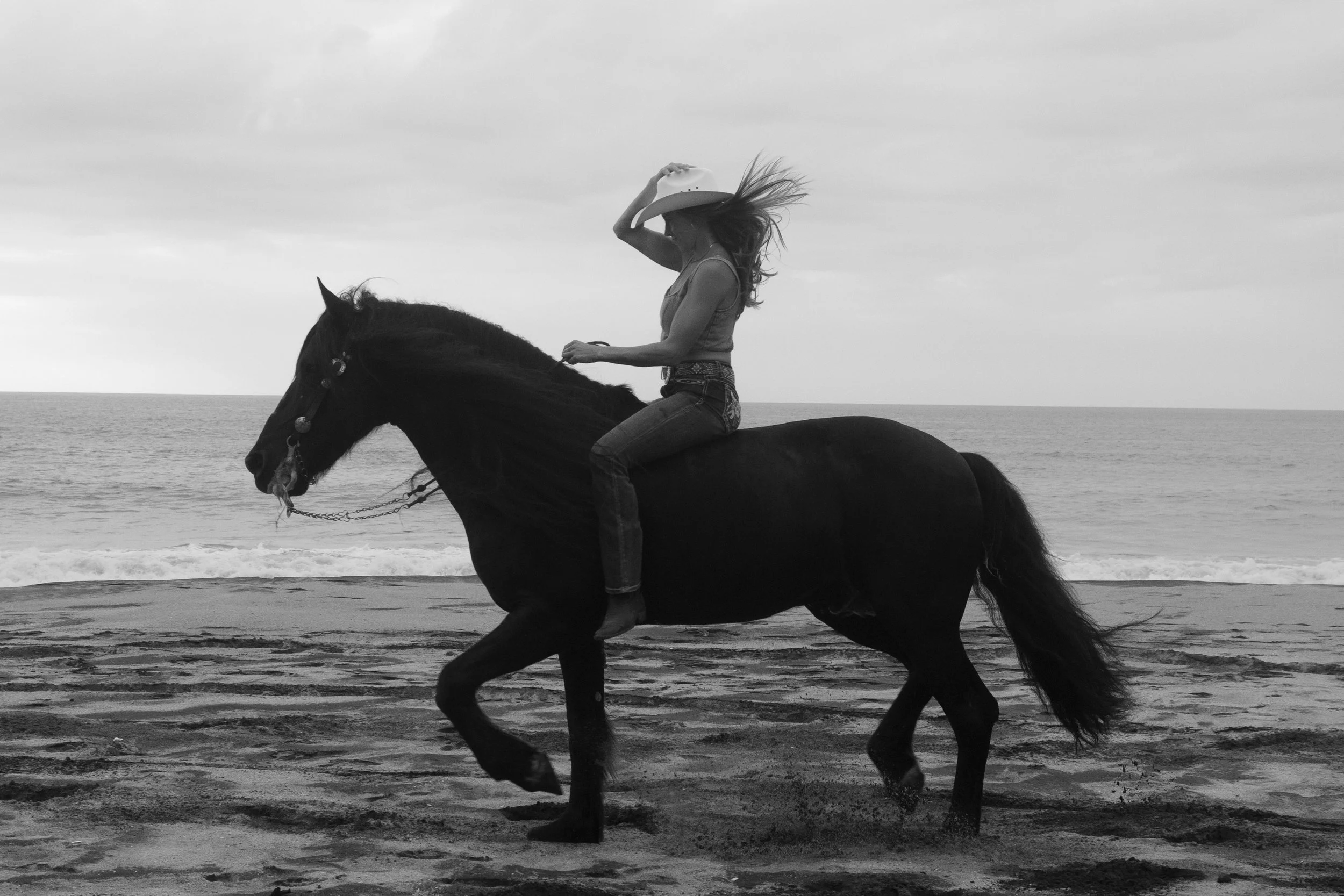 A woman riding a horse on the beach during the daytime.