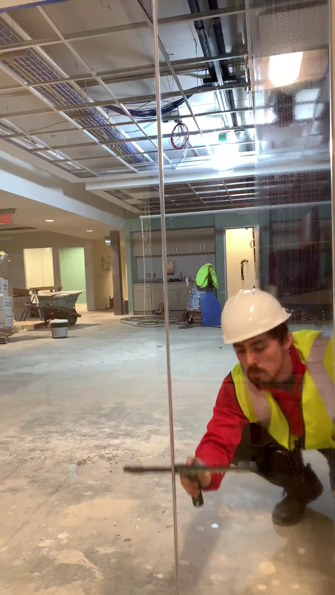 Professional window cleaner in a red uniform with a safety vest, behind a freshly cleaned pane of glass, on a construction site