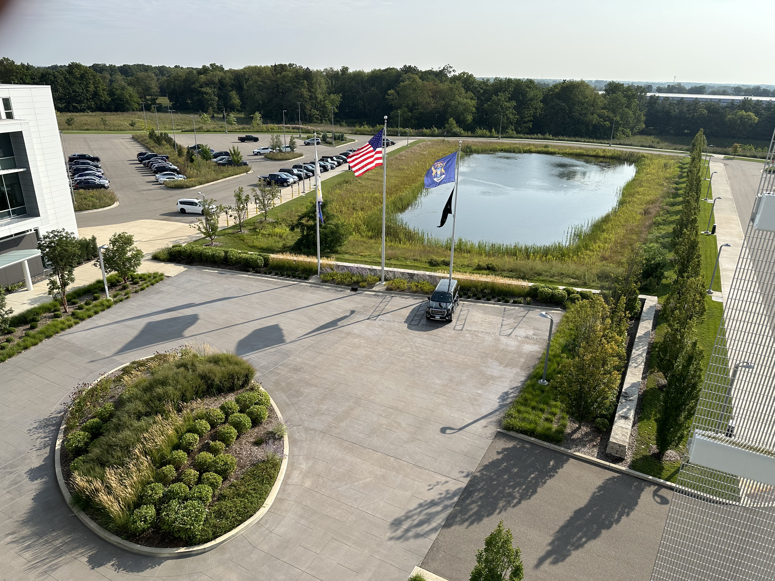 View from the top of a building, overlooking a pond, parking lot, and 3 flagpoles