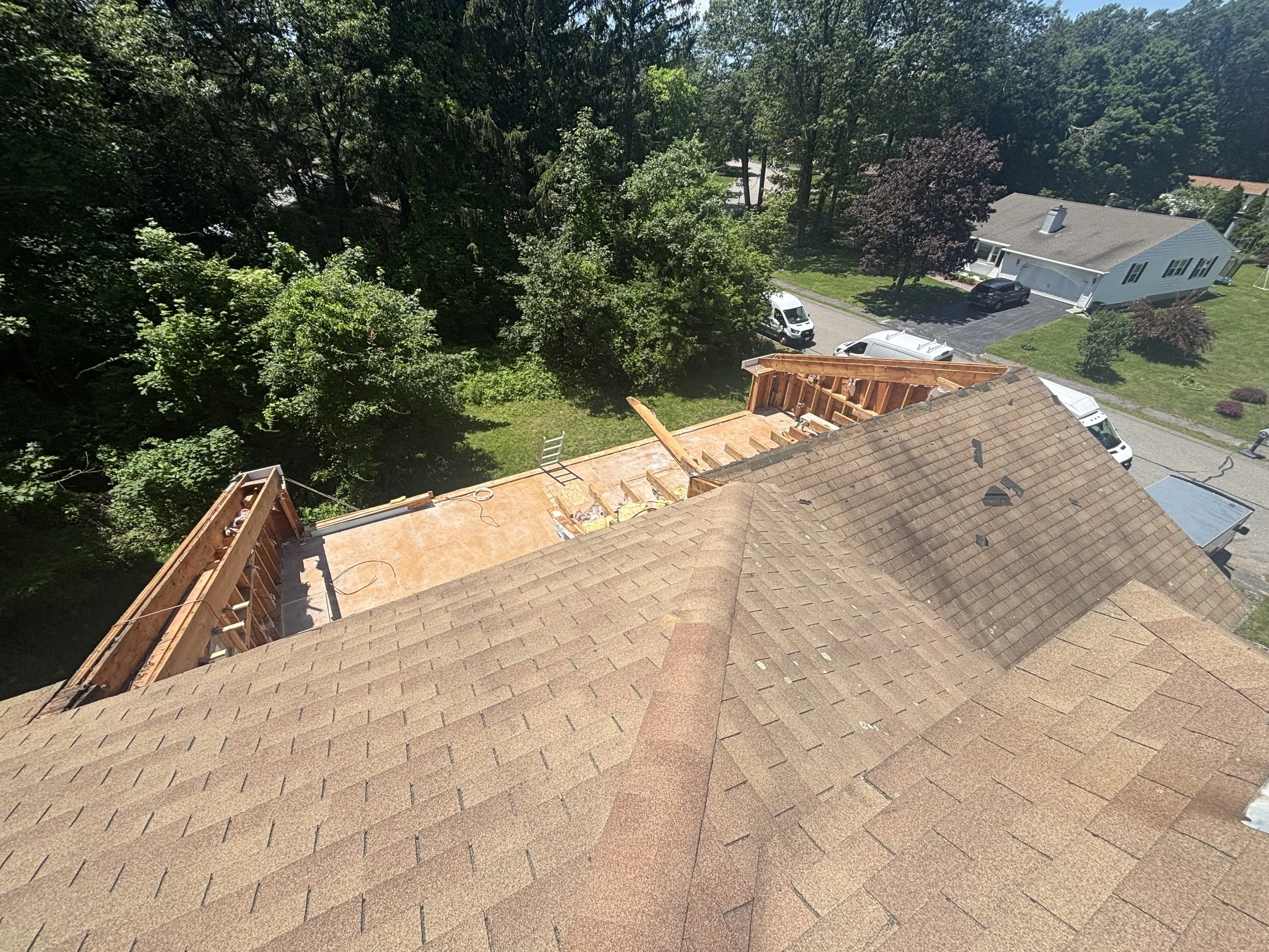 Aerial view of a residential backyard with a deck under construction, a house, parked cars, and trees.