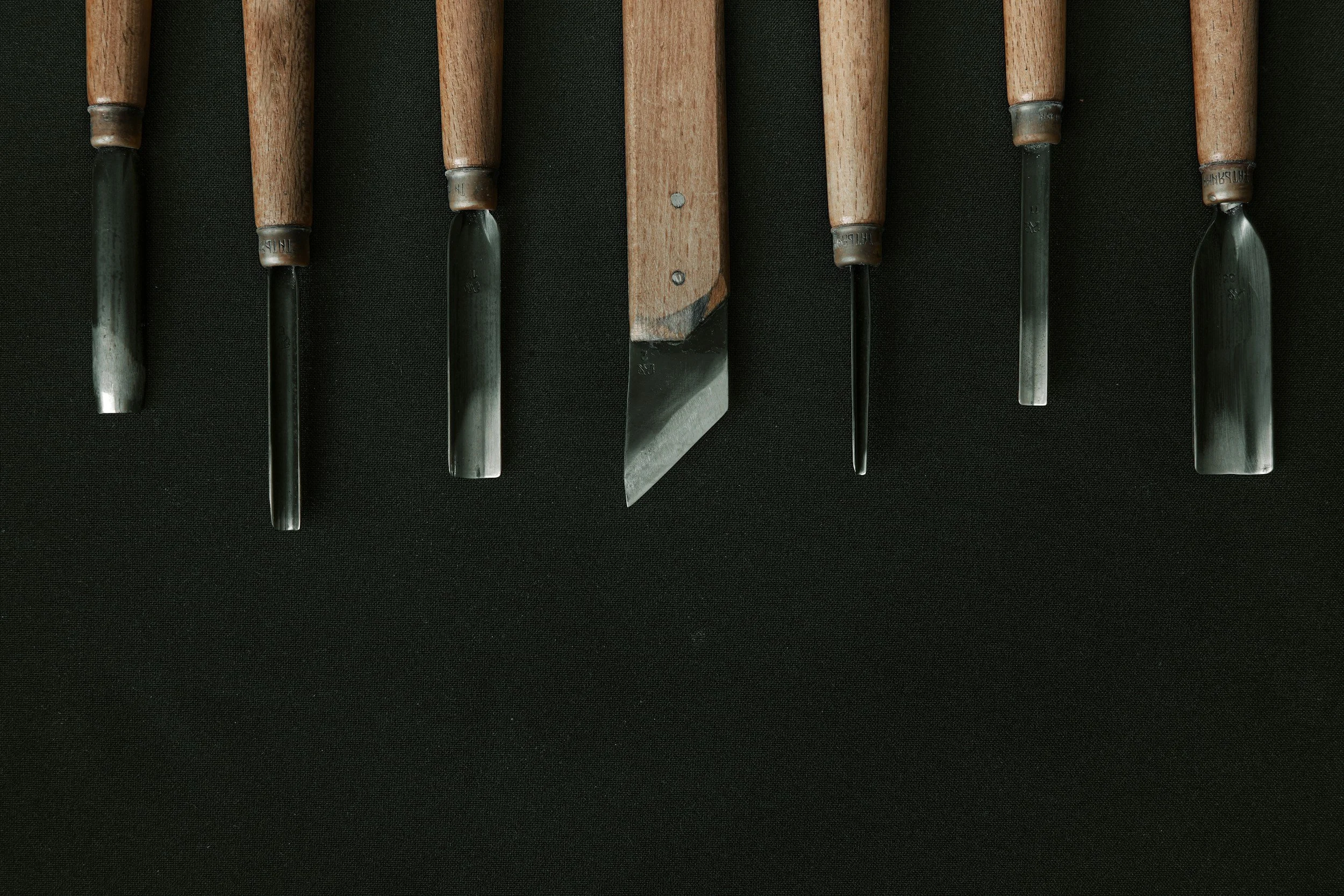 A row of chisels with wooden handles laid on a black surface.