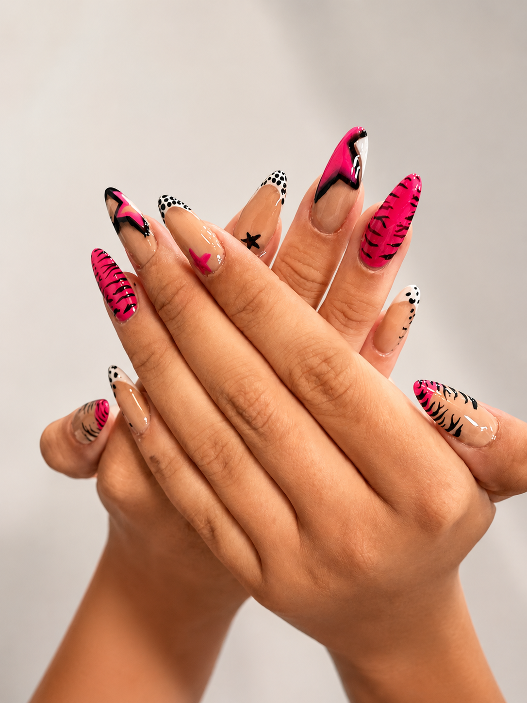 Close-up of hands with colorful, animal-inspired nail art including zebra and leopard patterns in pink, black, and nude shades.