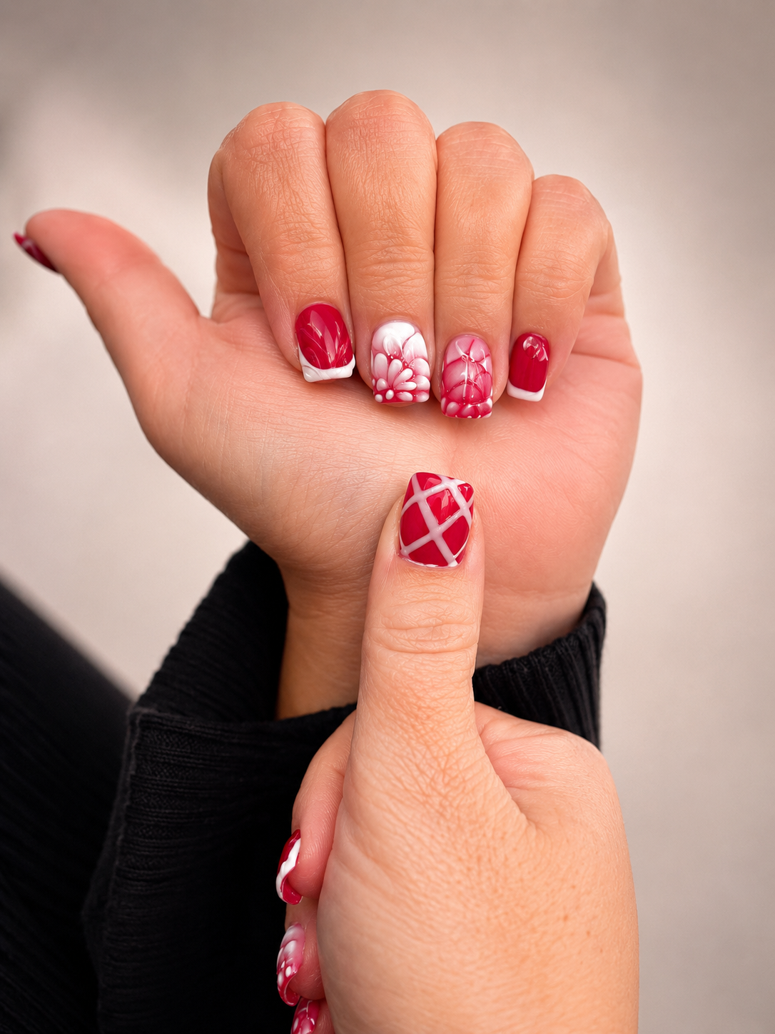 Close-up of a person's hand with red and white decorated nails, holding their other hand to show a matching finger nail design.