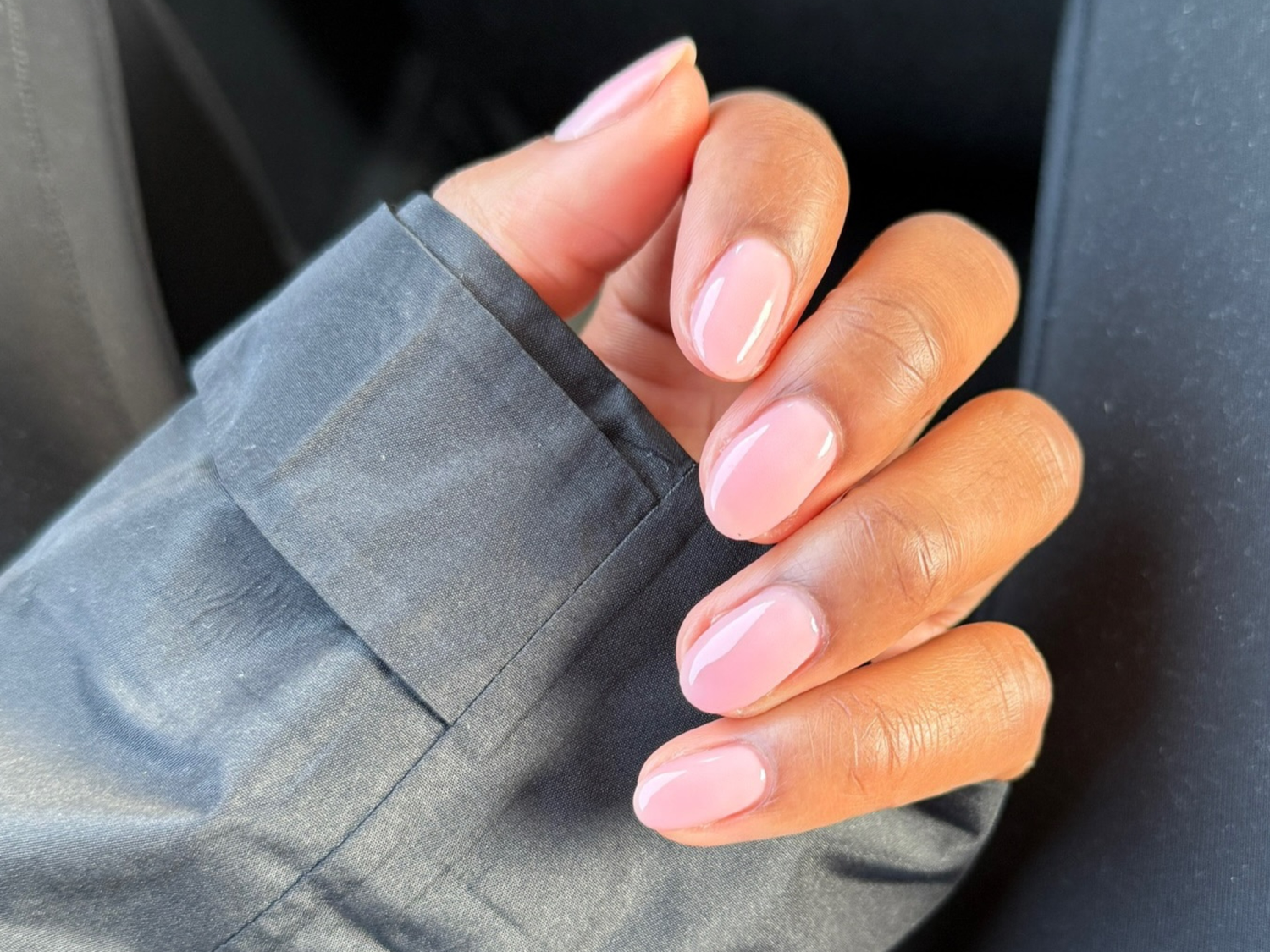 Close-up of a hand with well-manicured, glossy light pink nails, partially covered by a gray fabric sleeve.