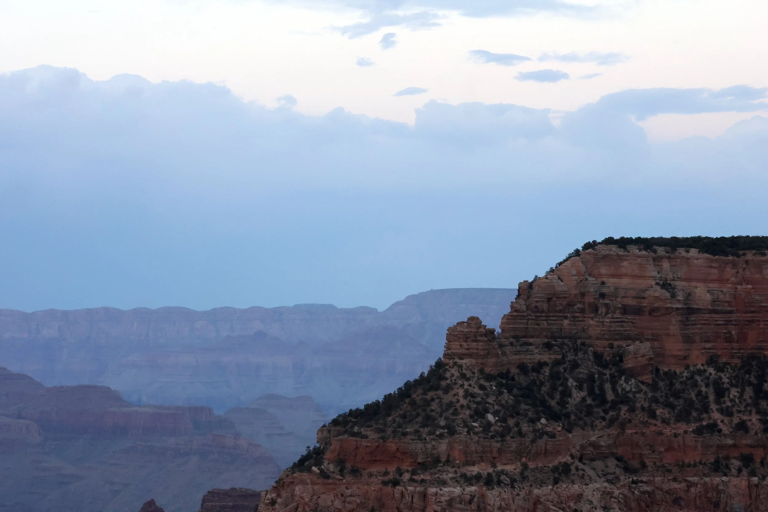 Landscape view of the Grand Canyon showing layered rock formations and a cloudy sky.