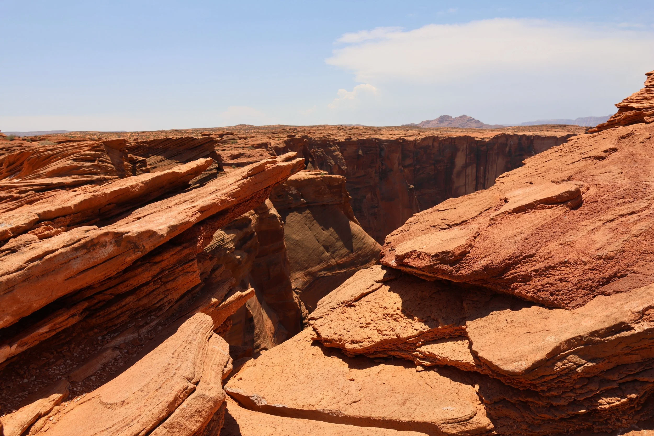 Red rock formations and canyons in a desert landscape under a partly cloudy sky.