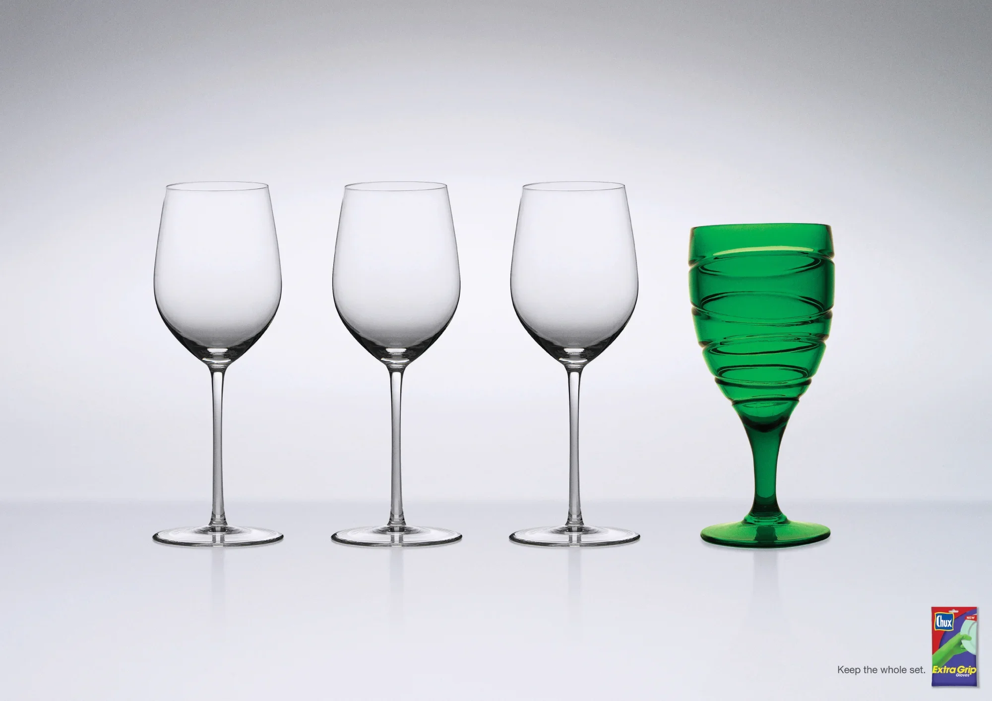 Three clear empty wine glasses with long stems and a green plastic cup in a spiral shape on a white background.