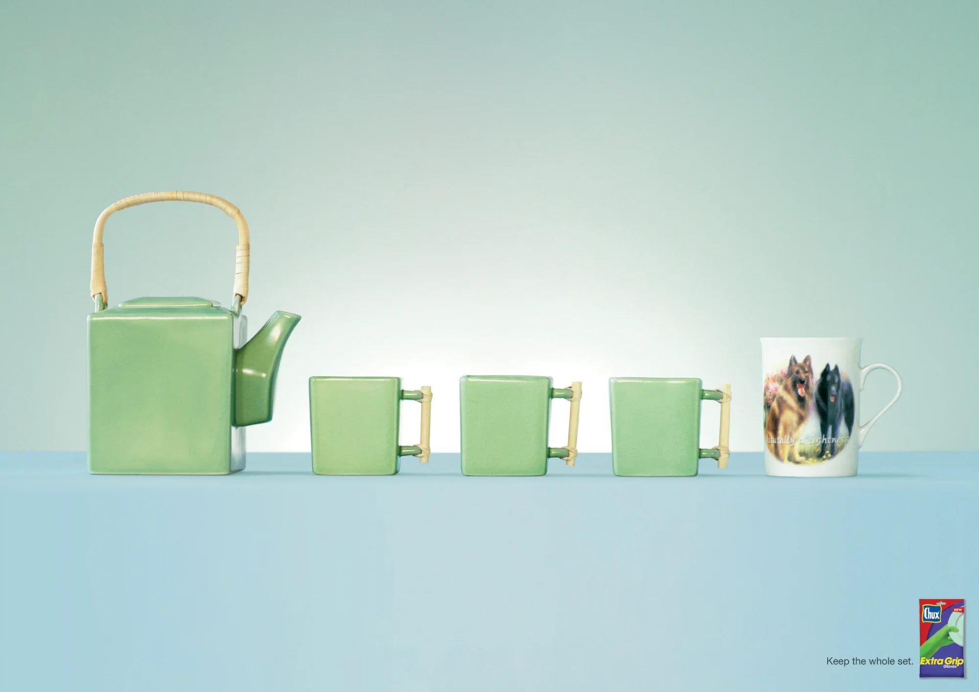 A green teapot and four matching green cups with bamboo handles are arranged in a row, with a white mug featuring a dog and a black cat, on a pastel blue surface against a pastel green background.