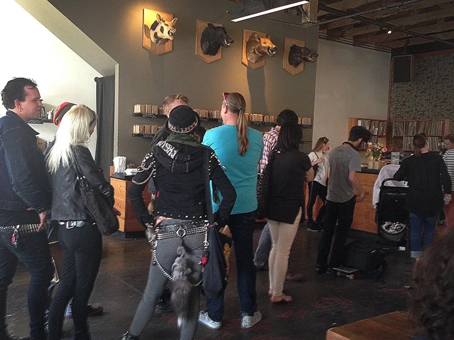 Group of people waiting in line at a restaurant or cafe with mounted animal heads on the wall.