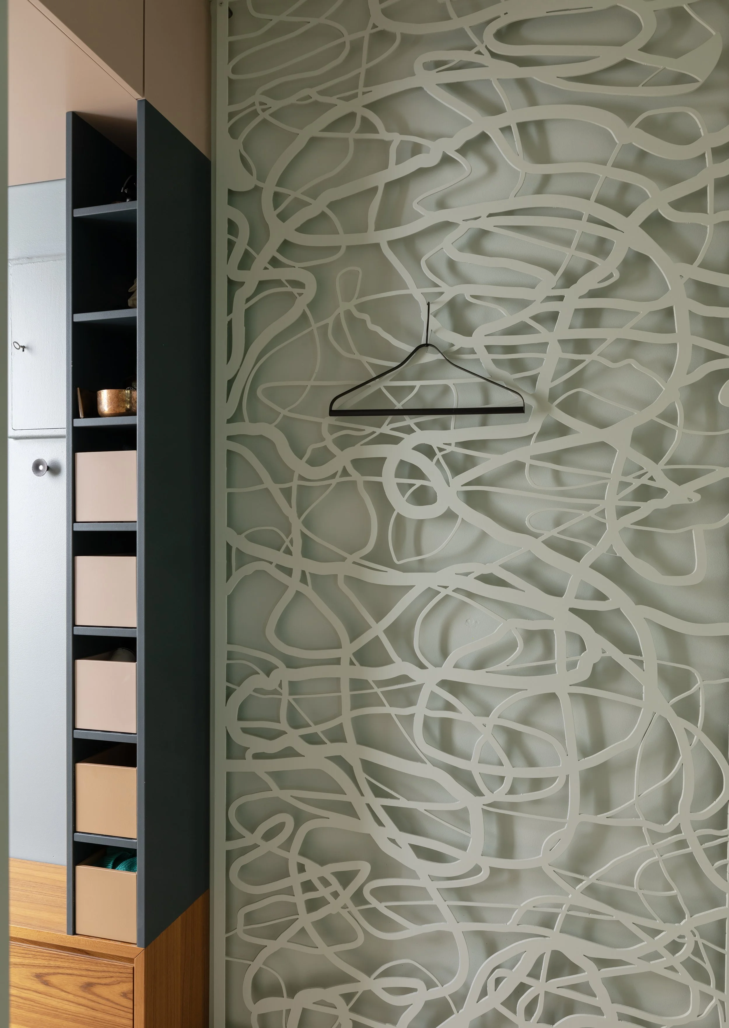 Interior space featuring a decorative wall partition with an abstract, swirling pattern, positioned next to a multi-colored shelving unit with open compartments and various objects inside.