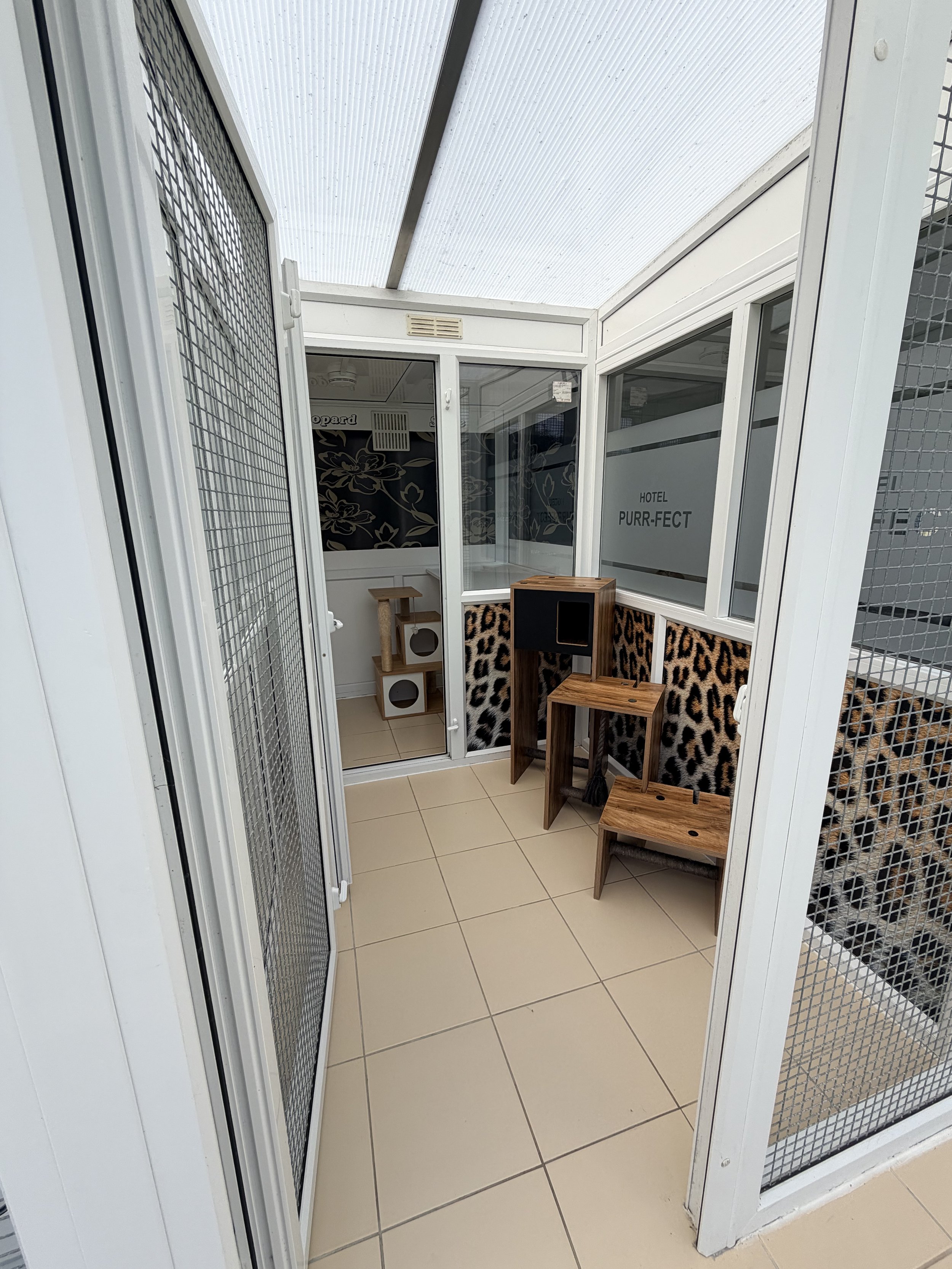 Small pet grooming or veterinary area with a closed door and some wooden furniture, leopard print fabric, and a sign that reads 'Hotel Purr-fect'.
