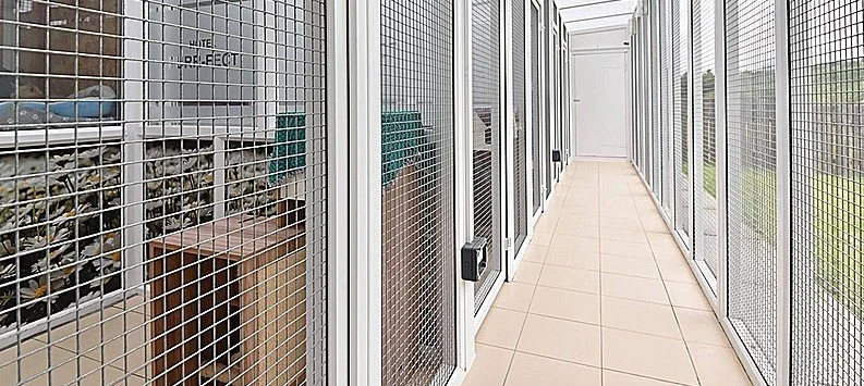 Long enclosed balcony with glass walls and a tiled floor, featuring a row of small animal cages or enclosures along the left side.