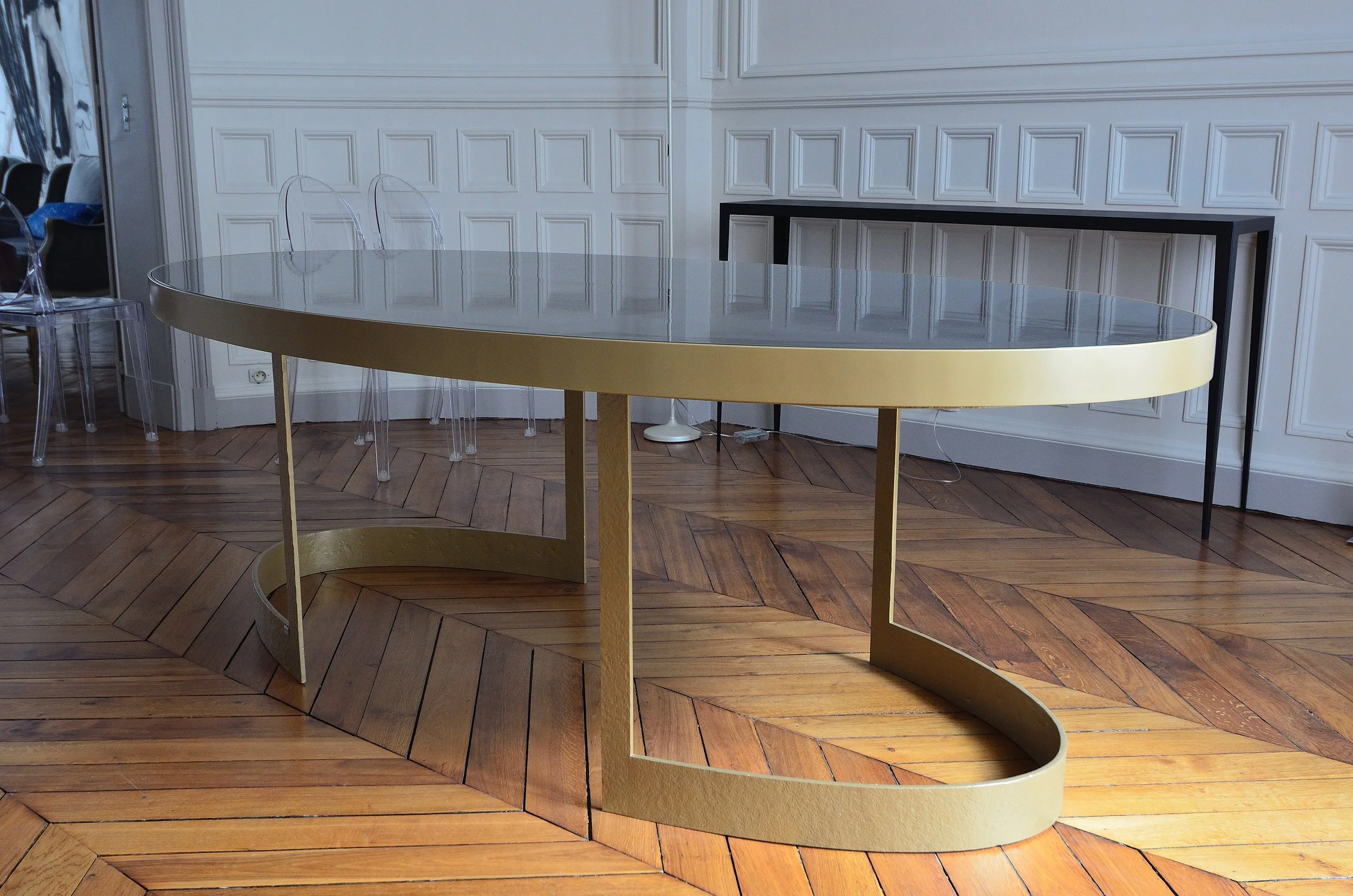 Une table en verre avec un cadre doré dans une pièce élégante avec des murs en bois gris et un parquet en bois foncé.