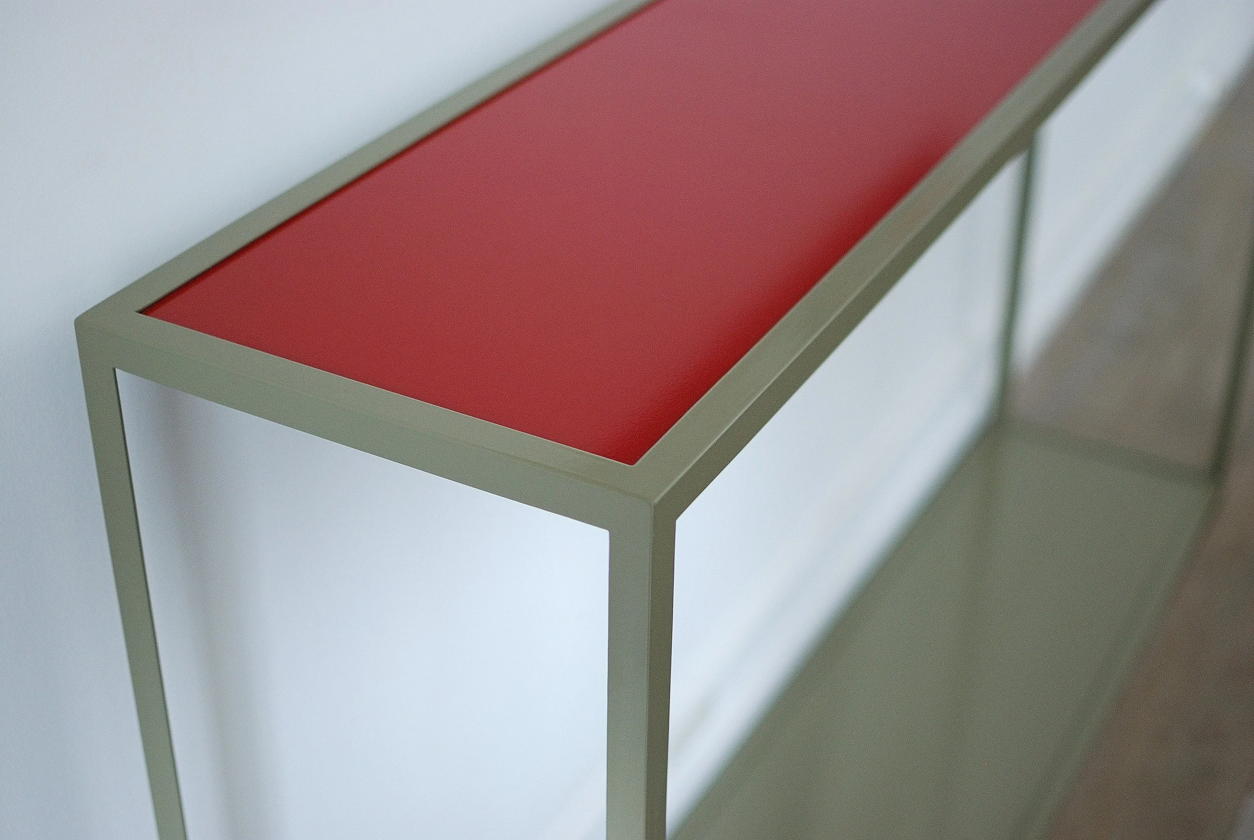 Tablette rectangulaire avec cadre en métal gris clair et surface rouge, placée contre un mur blanc.