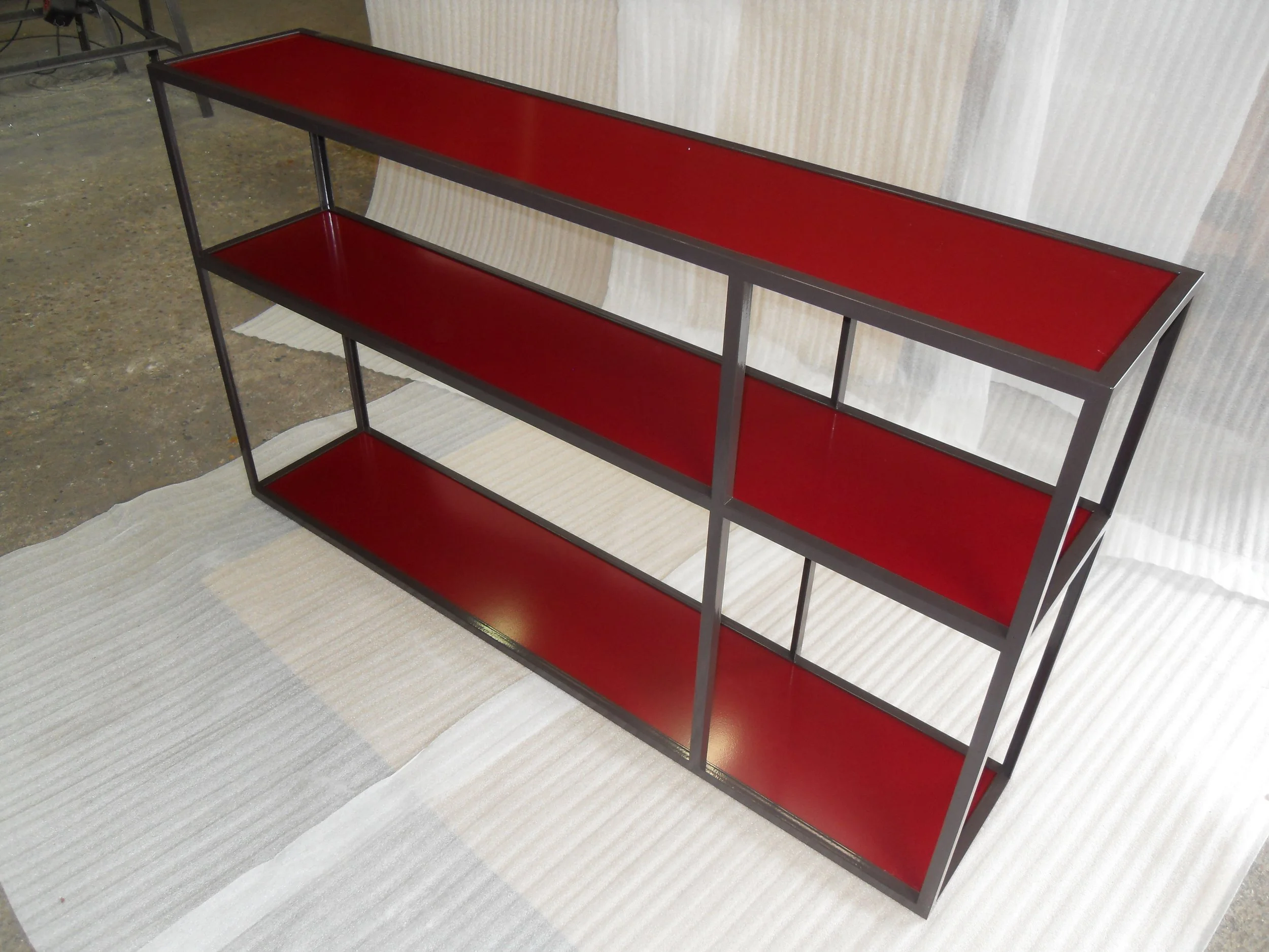 Une étagère moderne avec une structure en métal noire et des étagères en bois de couleur rouge.