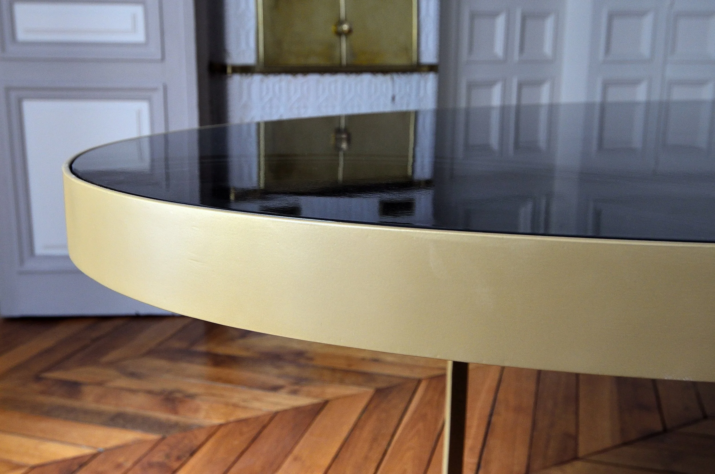 Table avec surface noire brillante et structure jaune, placée devant des portes de placard en bois clair, posé sur un sol en parquet.