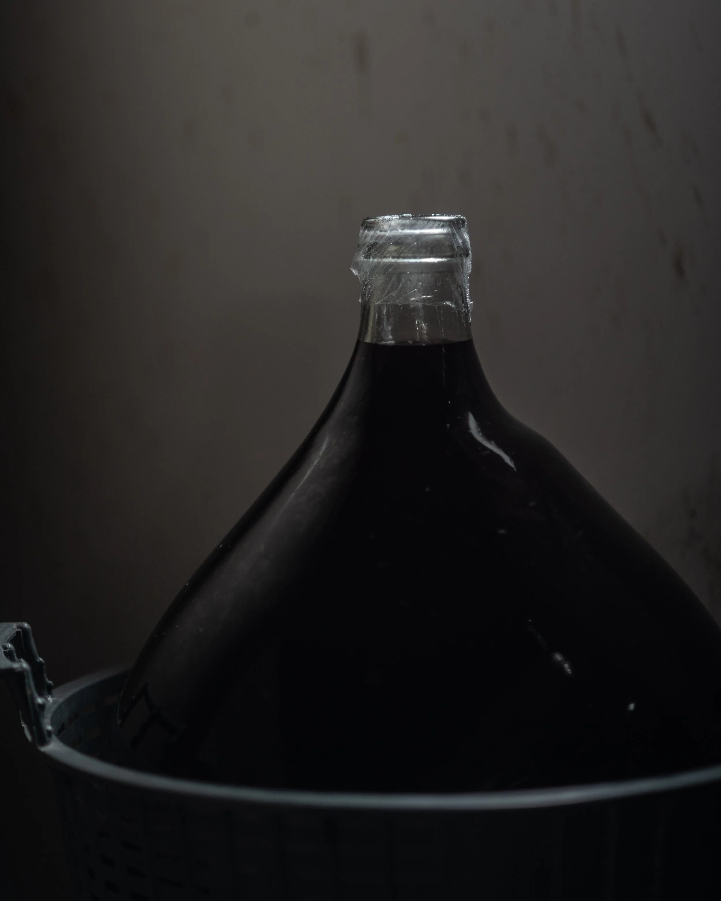 Close-up of the top of a dark glass bottle with a plastic cap, against a dark, blurred background.