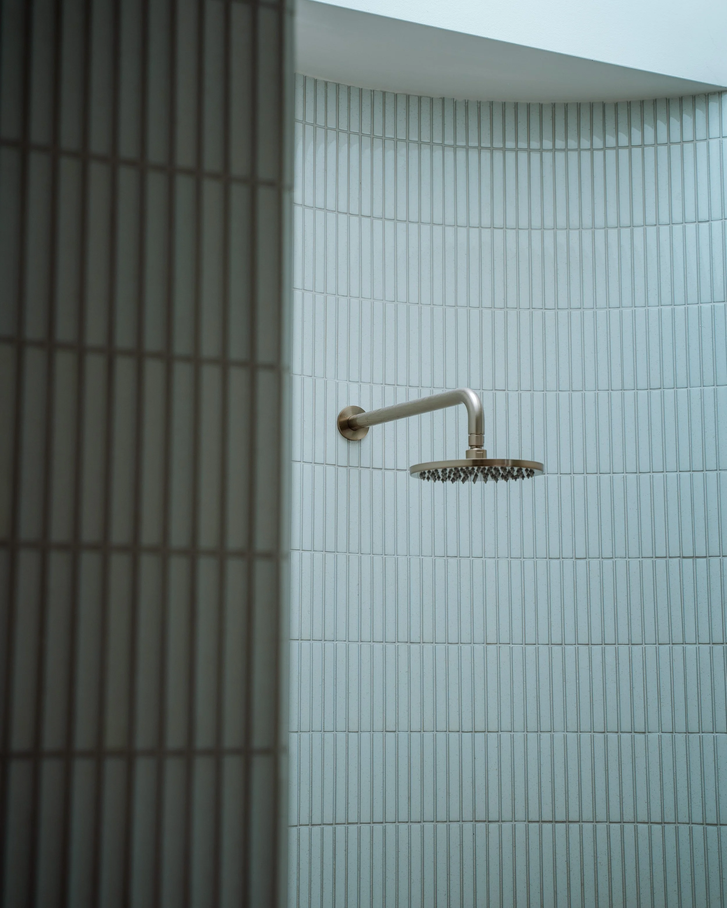 A shower area with tiled walls, a handrail, and a shower head visible from a unique angle.