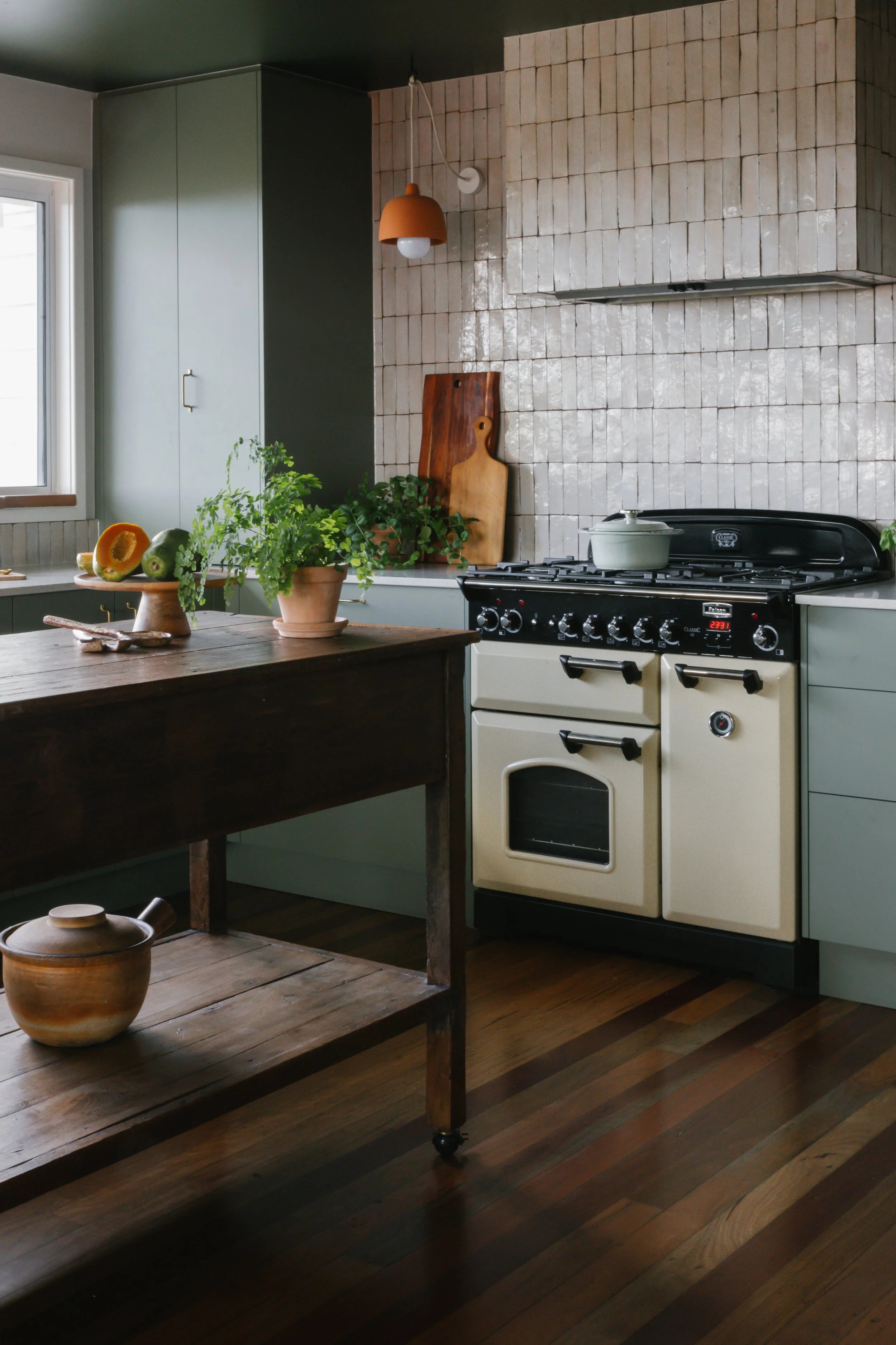Amber and Britt’s renovated kitchen in Terranora, featuring green cabinetry, handmade zellige tiles, a freestanding vintage timber island and ocean views.
