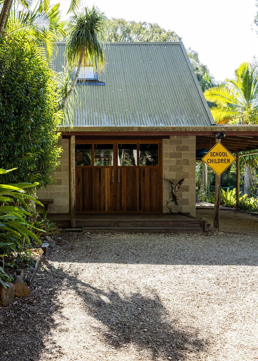 Exterior of the renovated Middle Pocket School House, featuring a corrugated metal roof, timber doors, tropical gardens and original School Children sign.