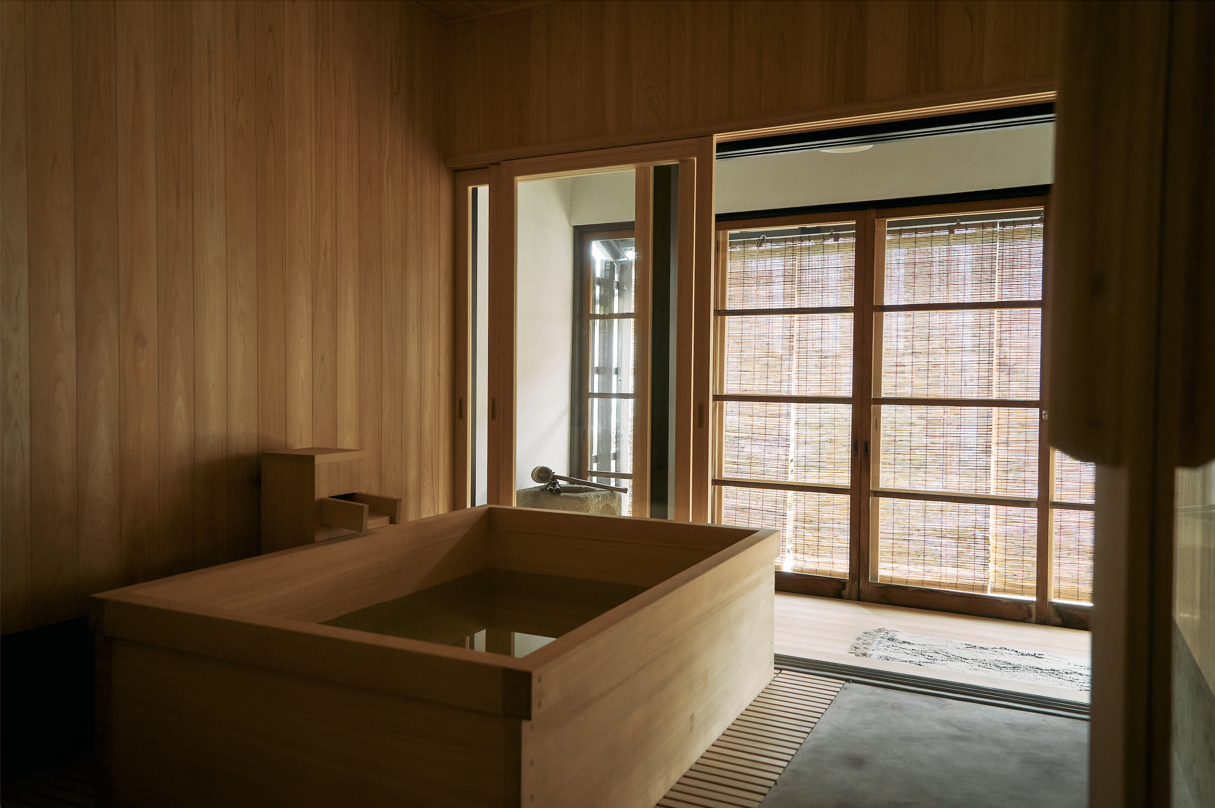 Interior of a room with hinoki paneling, a hinoki soaking tub, ofuro,  and large windows with bamboo blinds called sudare