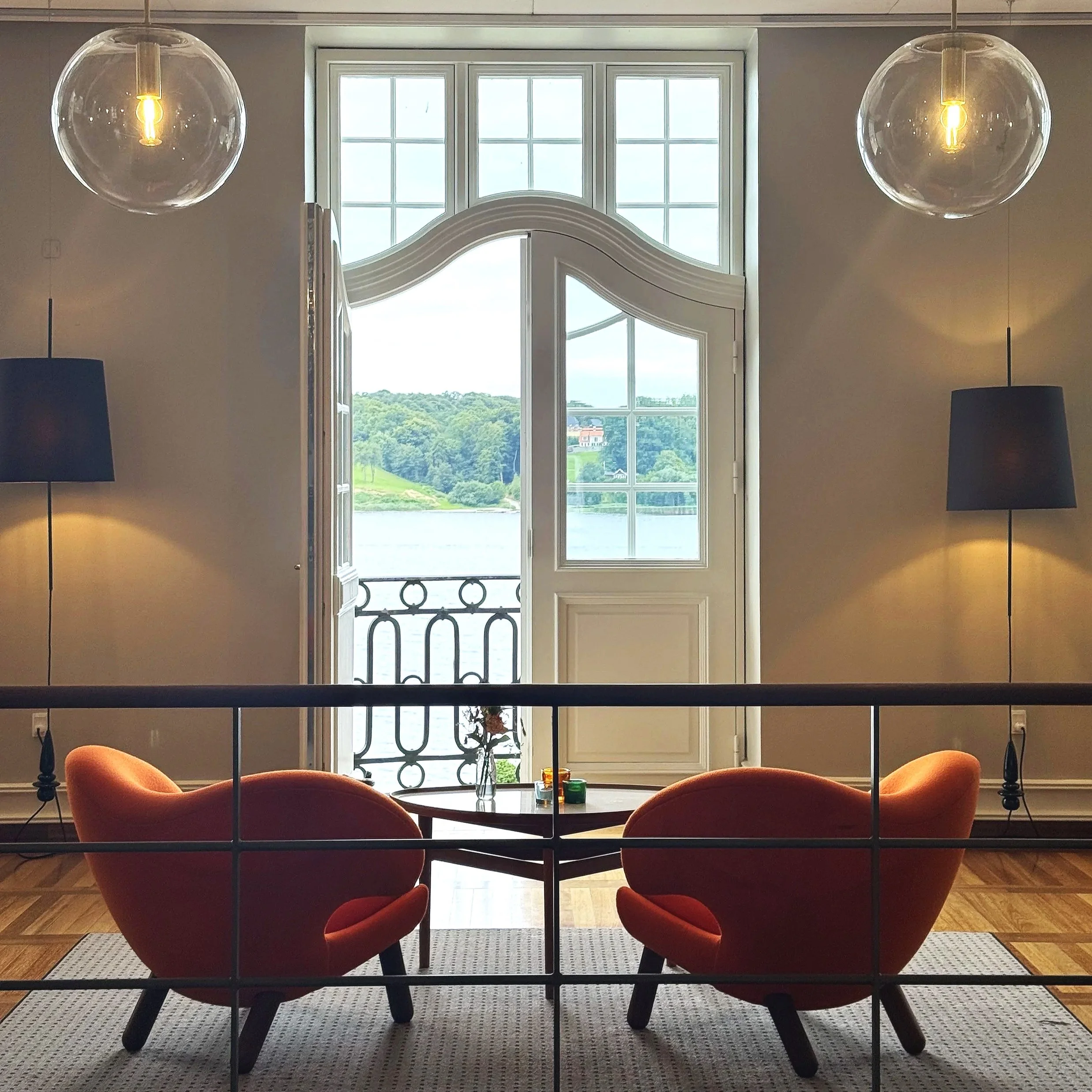 Living room with large window, three orange chairs around a round table, and two hanging glass light fixtures.