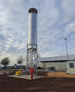 Industrial smokestack next to a small building under a cloudy sky.