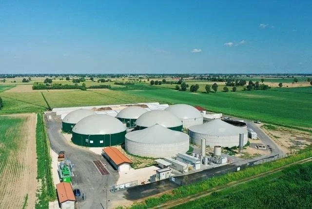 Aerial view of a biogas plant with multiple large white domed digesters surrounded by green farmland.