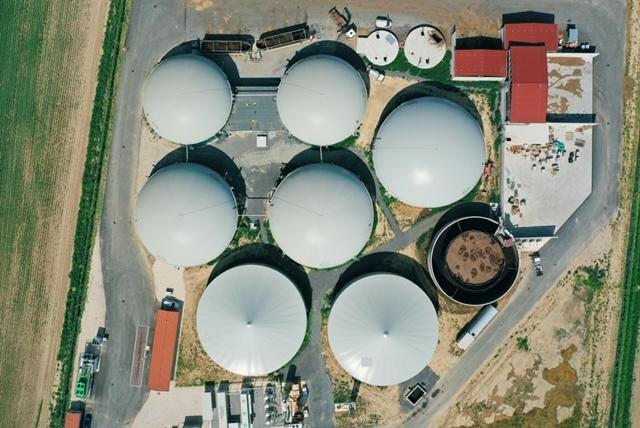 Aerial view of a facility with multiple large white storage tanks, some with black tops, surrounded by buildings, equipment, and a rural landscape.