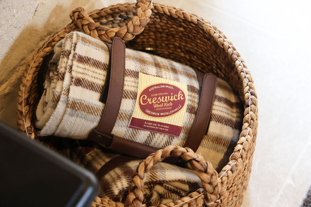 A woven basket containing a package of Creswick Wool Rich wool, wrapped in a plaid fabric with shades of cream, brown, and tan.