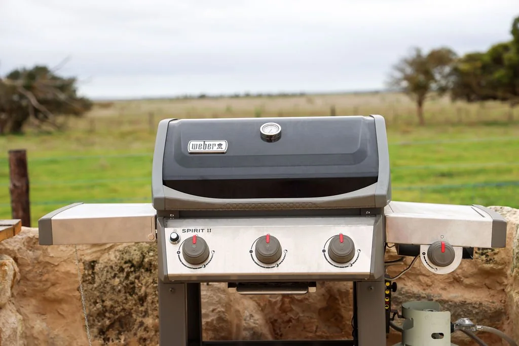 A Weber Spirit II gas grill on a stone surface outdoors with a rural landscape in the background.