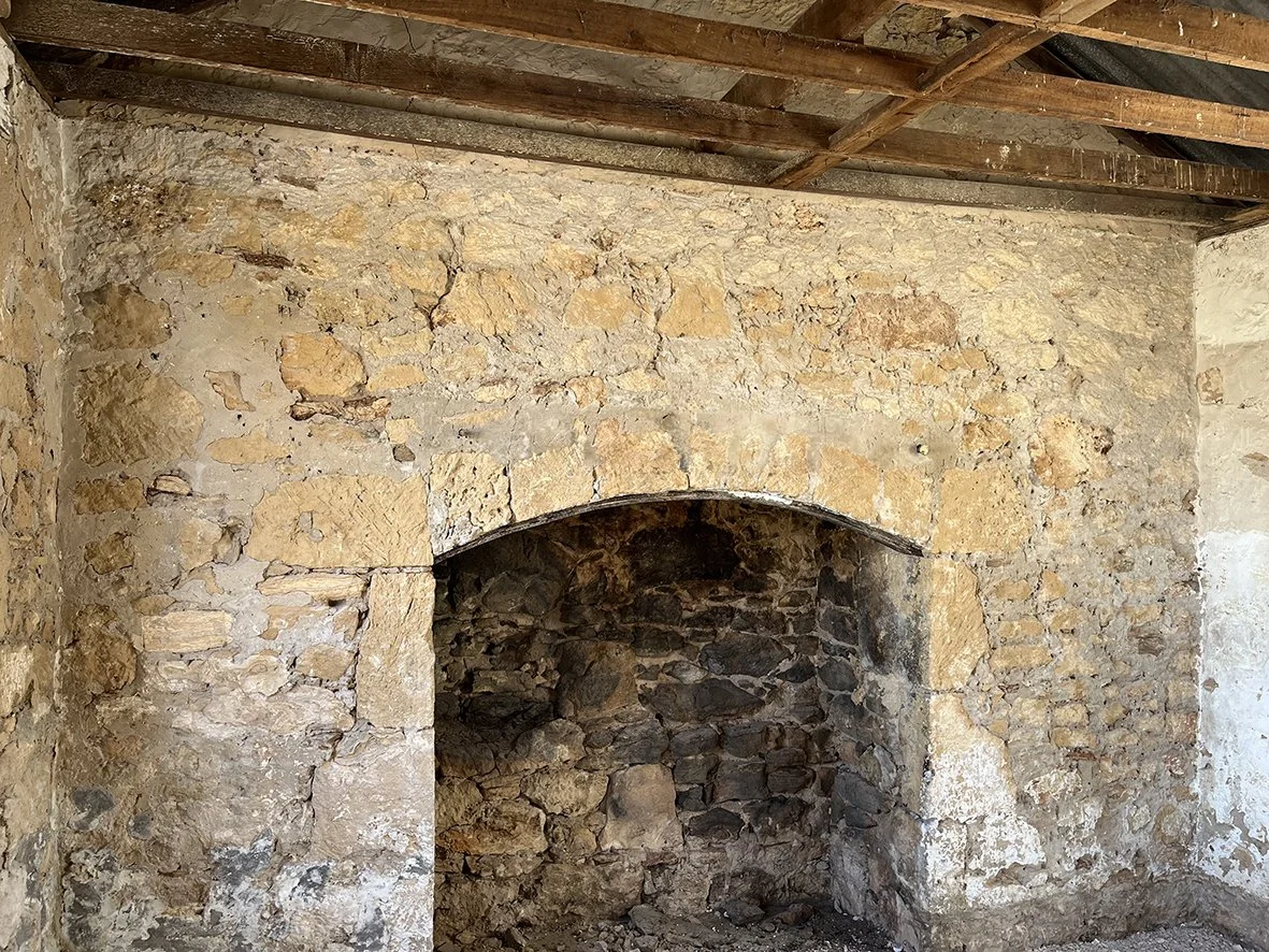 Interior of an old stone fireplace with a wooden beam ceiling.