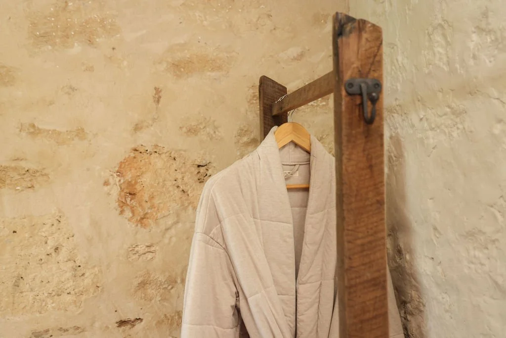 A beige bathrobe hanging on a wooden hook against a textured stone wall.
