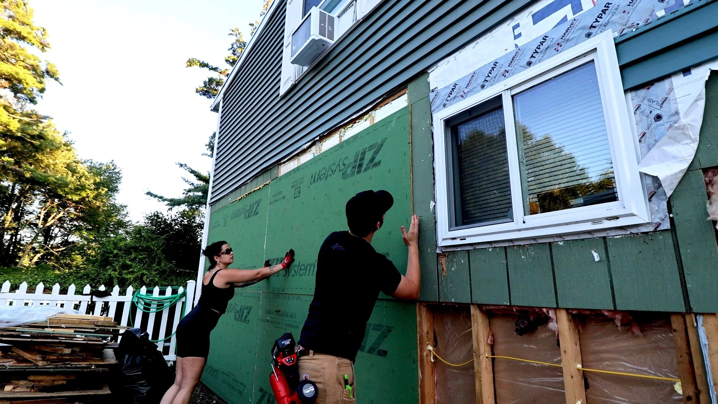 Two people DIY installing zip sheathing on a home renovation project