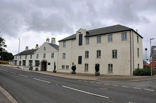 A white building and a church with chimneys on a cloudy day, located along a street with a 30 mph speed limit sign.