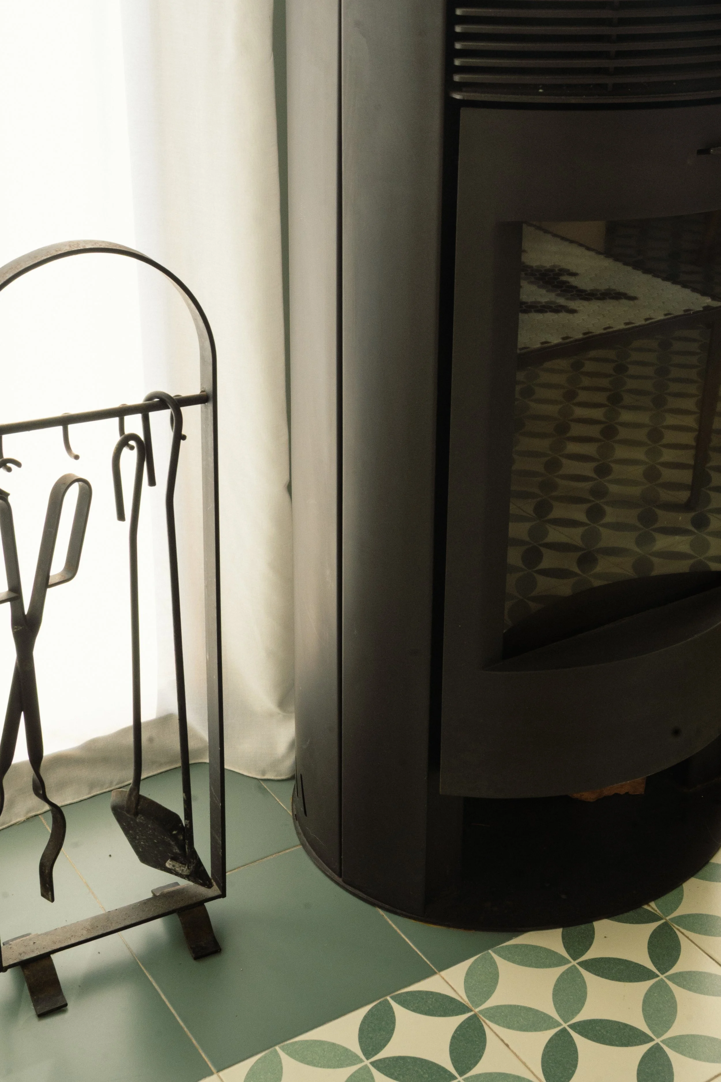 Estufa de microondas negra en una encimera y soporte para utensilios de cocina hecho de metal con hatillos en la parte izquierda, en un piso de baldosas con diseño de círculos y hojas verdes.