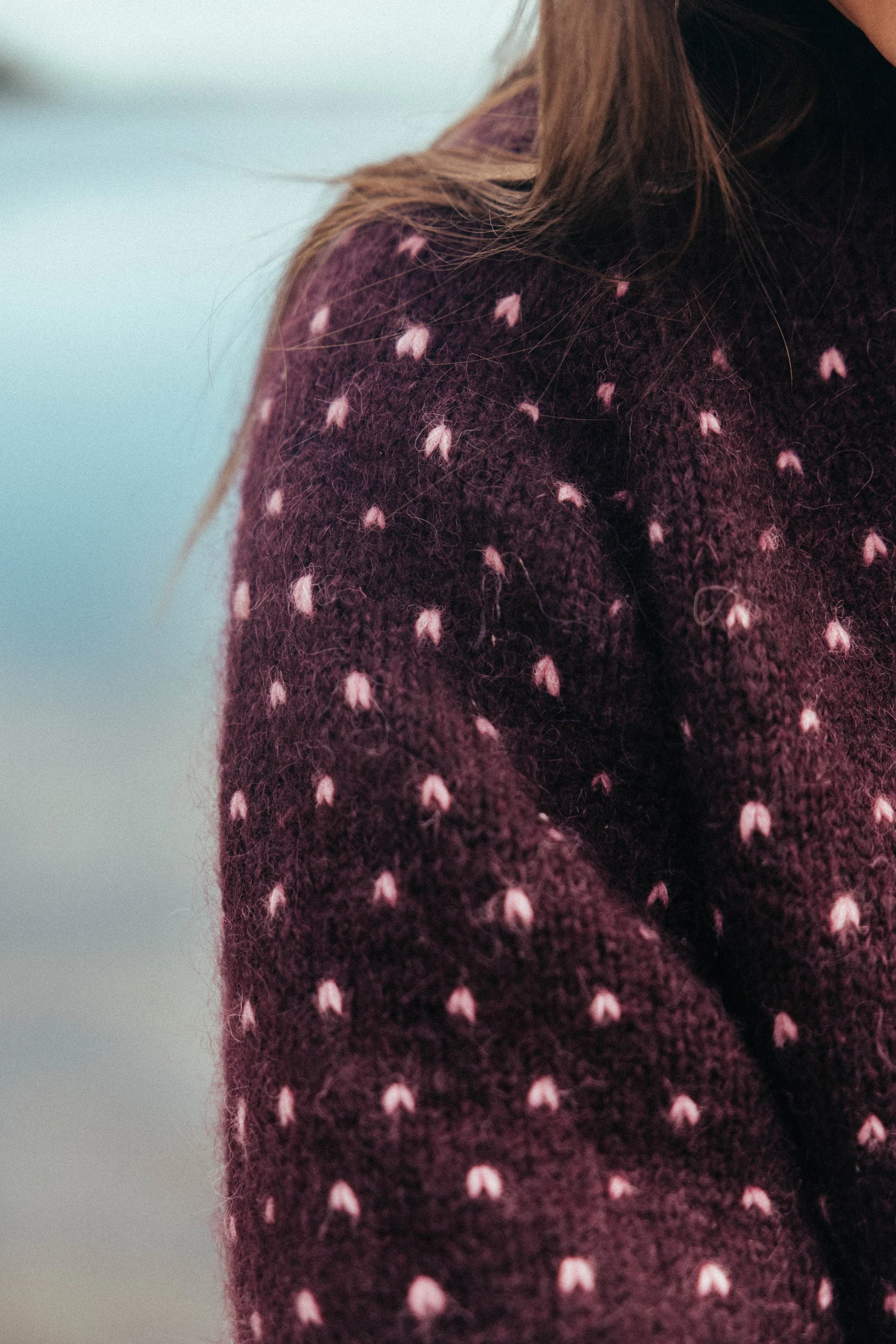 Nærbillede af en person med brunt hår iført en lilla sweater med lyserøde prikker.