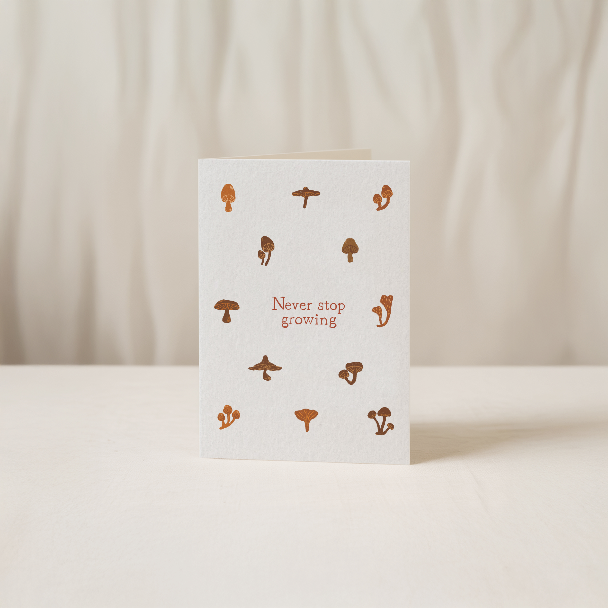 Minimalist greeting card featuring brown mushroom illustrations and the text Never stop growing, original art by Kadna Anda.