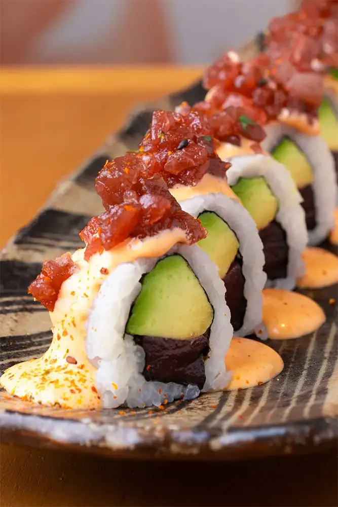 Rollitos de sushi con aguacate, cangrejo y salsa picante, cubiertos con salsa teriyaki y cebolla crispy, servido en un plato'}letic.105 in Soup, in a bowl on a white table, with sliced vegetables and herbs. The photo captures the aroma of the dish and the freshness of the ingredients.